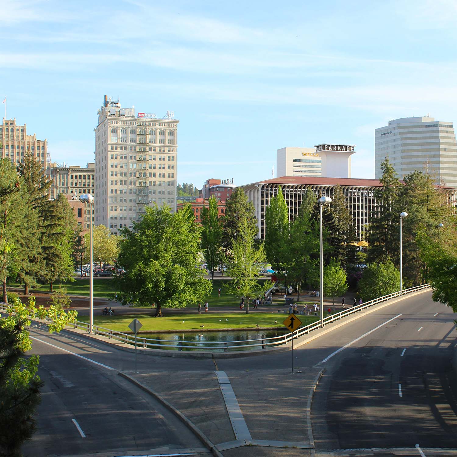 Downtown Spokane skyline behind a tree-filled park and small pond, with curving roads in the foreground.