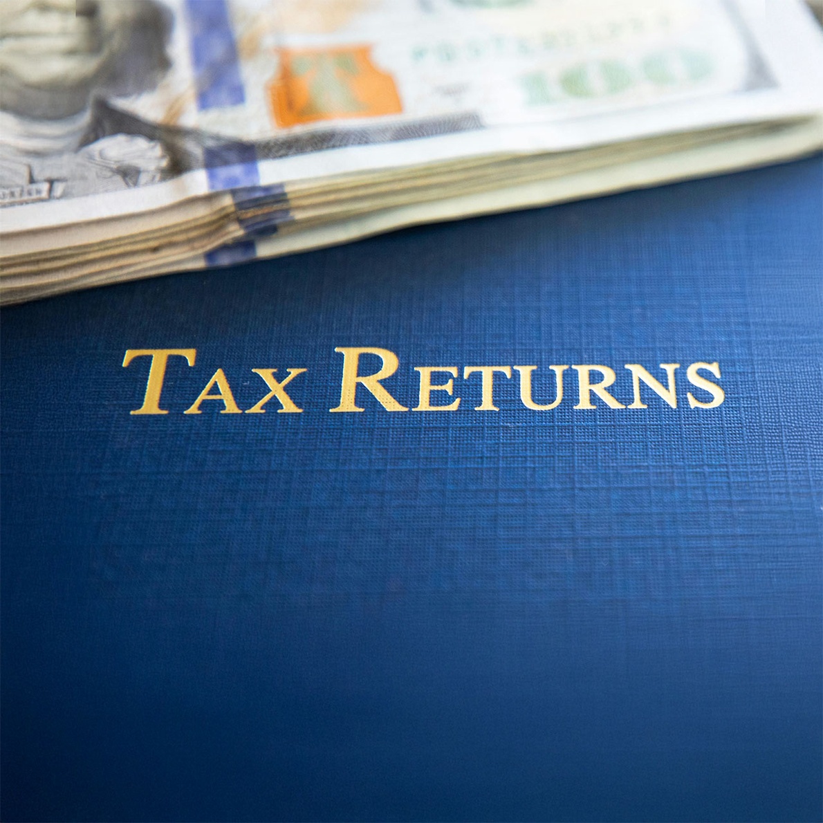 Tax returns document with gold lettering and stack of hundred-dollar bills on top