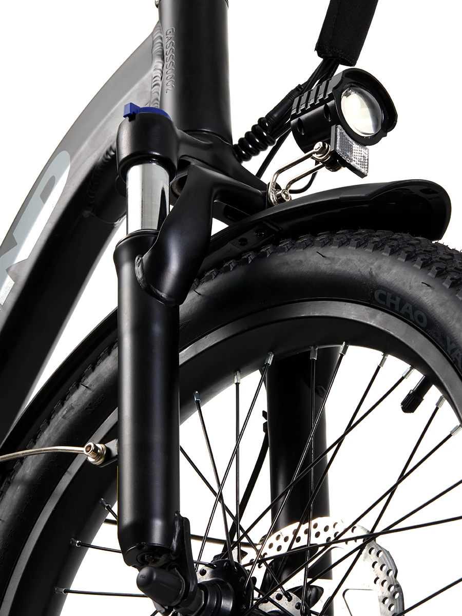 Close-up of an electric bicycle’s front suspension fork with shock absorbers, front headlight, fender, and disc brake system mounted on a rugged tire.