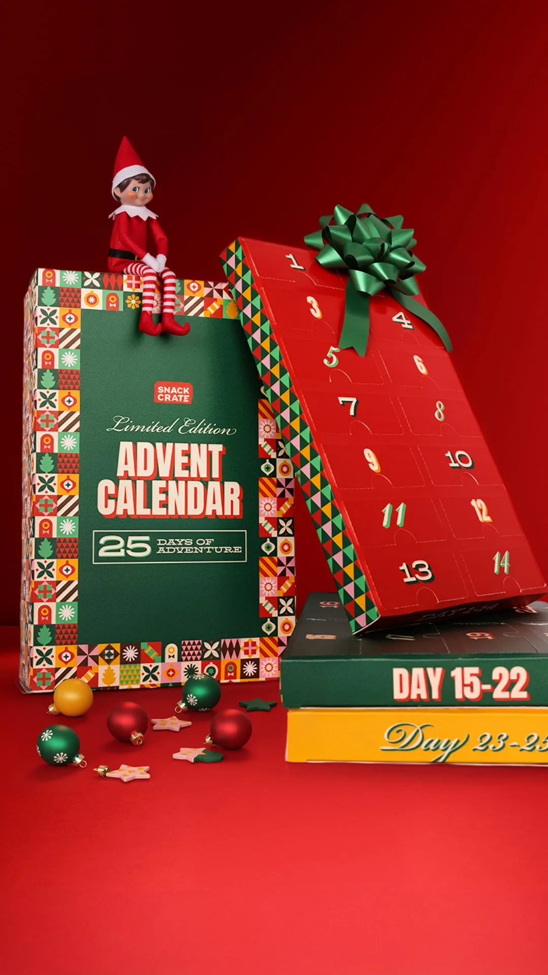Limited edition Snack Crate Advent Calendar with 25 days of adventure, featuring colorful numbered boxes, a green bow, Christmas ornaments, and an elf doll sitting on top.