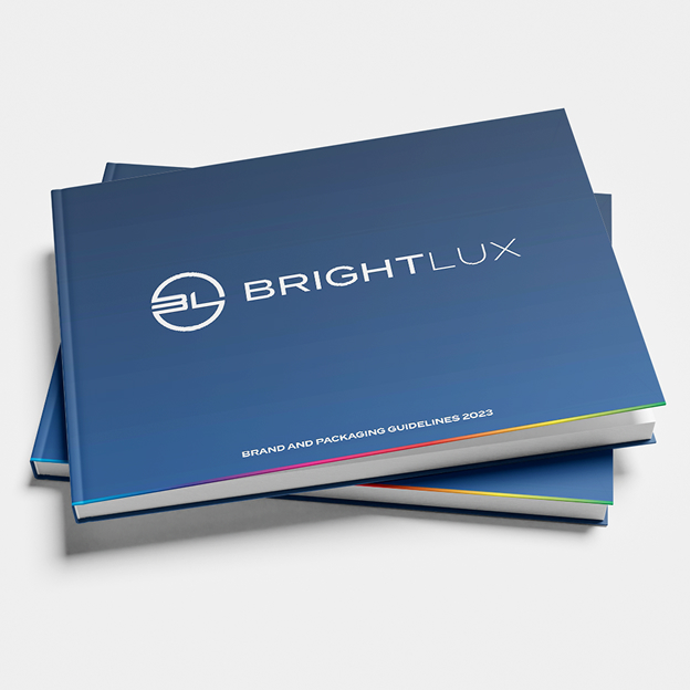 Stacked brand guidelines books with blue covers labeled BRIGHTLUX and BRAND AND PACKAGING GUIDELINES 2023.