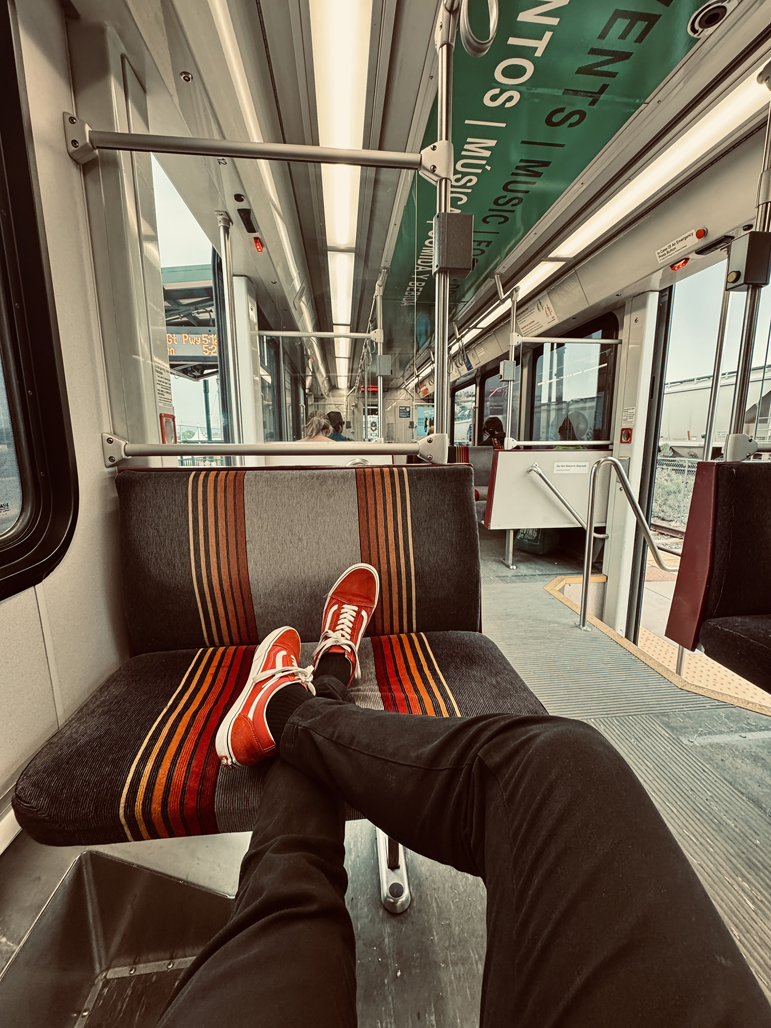 Person wearing red sneakers with white laces relaxing with legs stretched out on a striped patterned seat inside a train or tram.