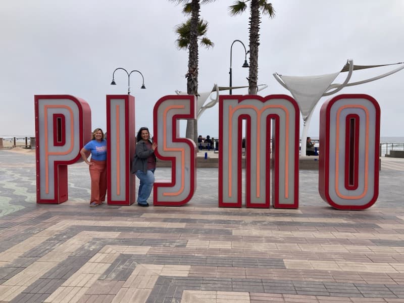 Sherri and a friend posing with the Pismo sign landmark in Pismo Beach. 