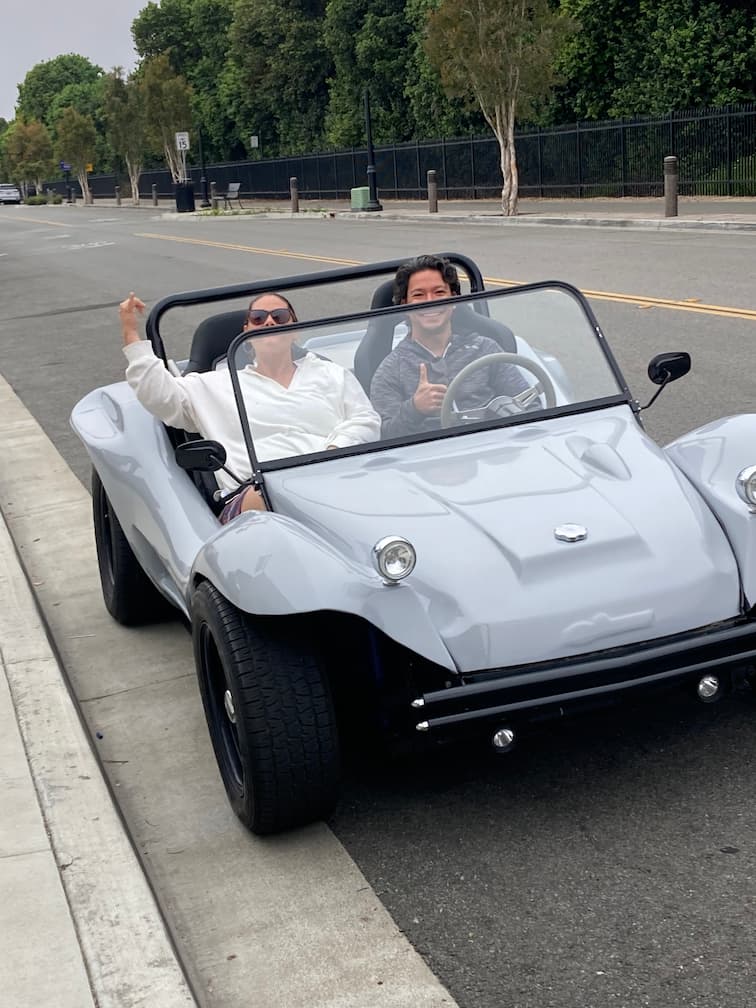 Two people driving an antique car and waving