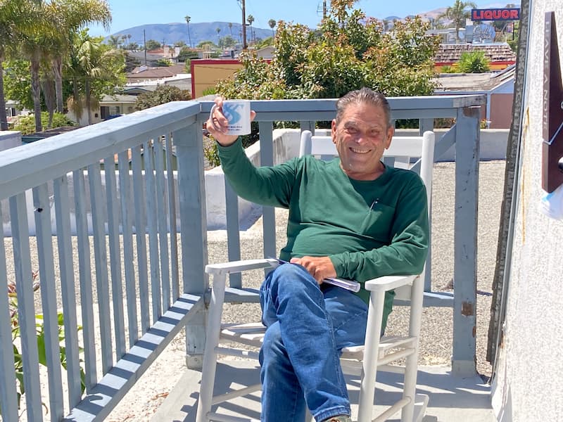 Man holding a Sherri Banta branded mug sitting on a balcony