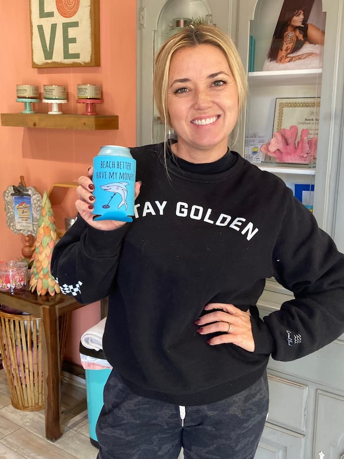 Young woman holding a drink wrapped in a Sherri Banta branded Koozie