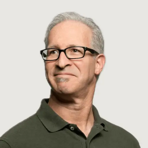 Middle-aged man with gray hair, glasses, and a small goatee, wearing a dark green polo shirt, looking slightly to the side with a neutral expression.