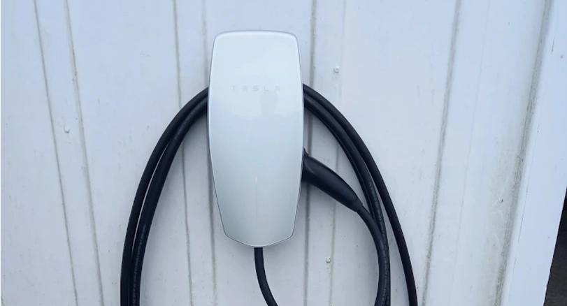 Tesla wall connector electric vehicle charger mounted on white weatherboard wall with charging cable