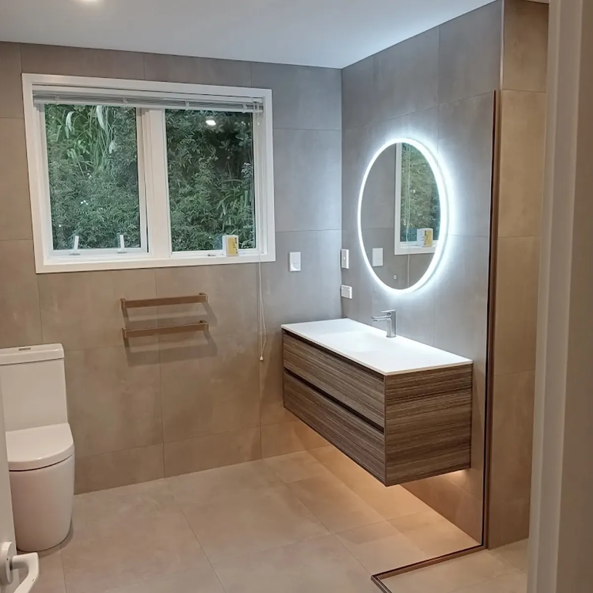 Modern bathroom with illuminated round mirror, floating vanity, and grey tile walls