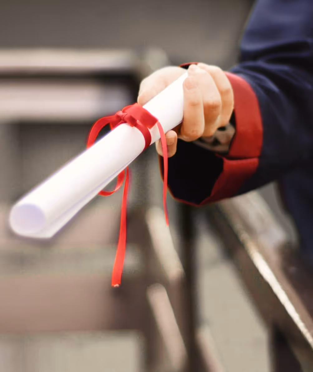 Hand holding a rolled-up diploma tied with a red ribbon.