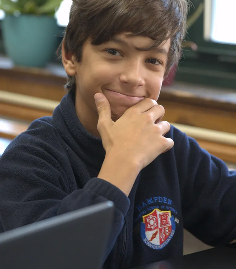 Smiling boy with dark hair resting his chin on his hand wearing a navy blue Hampden Academy jacket.