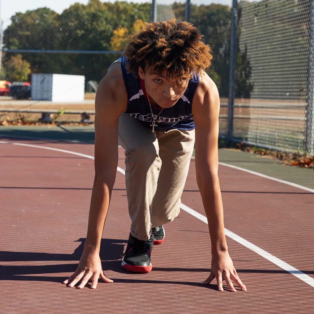 Young man in athletic stance on outdoor court preparing to sprint.