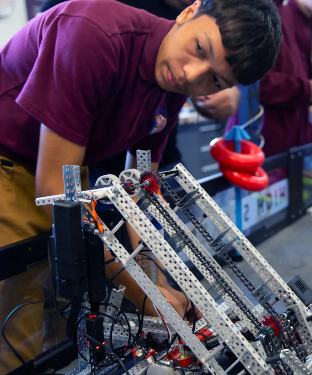 Young man in a maroon shirt working on a metal and chain robotics project indoors.