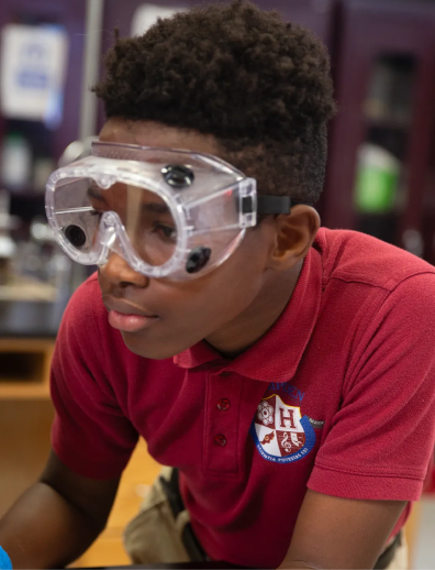 Student wearing clear protective goggles and a maroon polo shirt with a school emblem.