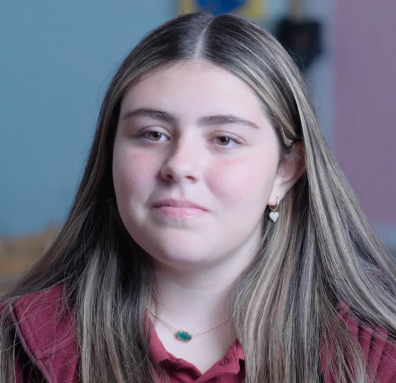 Portrait of a young woman with long dark hair wearing heart-shaped earrings and a pendant necklace.