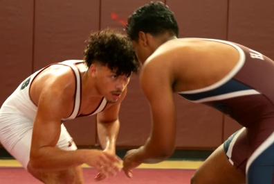 Two male wrestlers in singlets facing each other on a wrestling mat during a match.