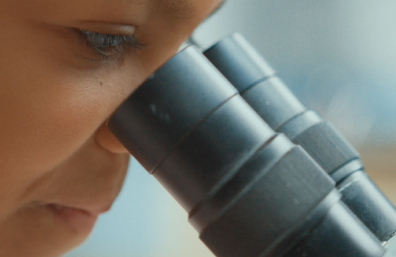 Close-up of a young person looking into a microscope.