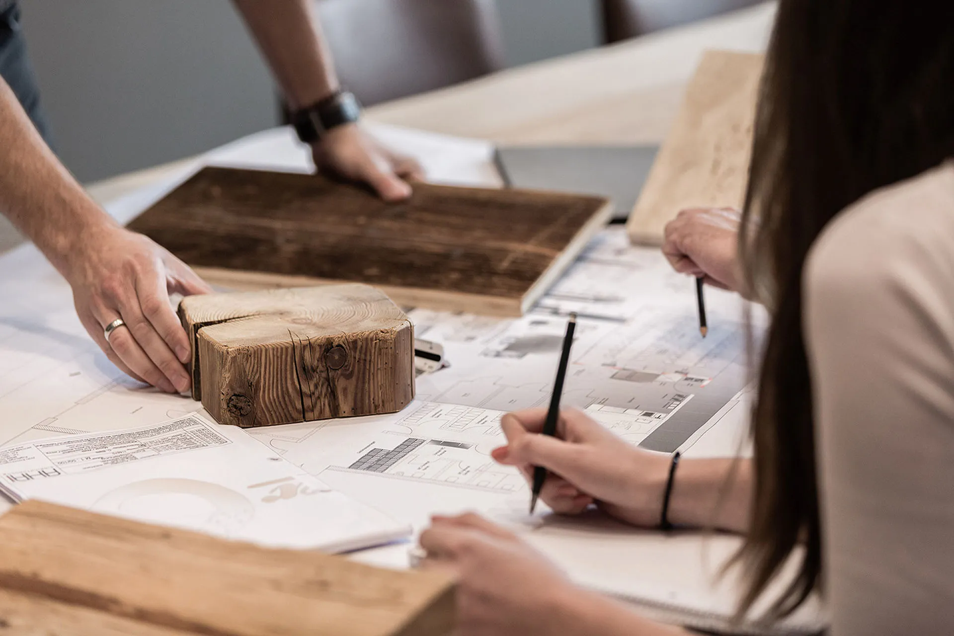 Verschiedene Materialmuster aus Holz werden auf einem Raumplan besprochen