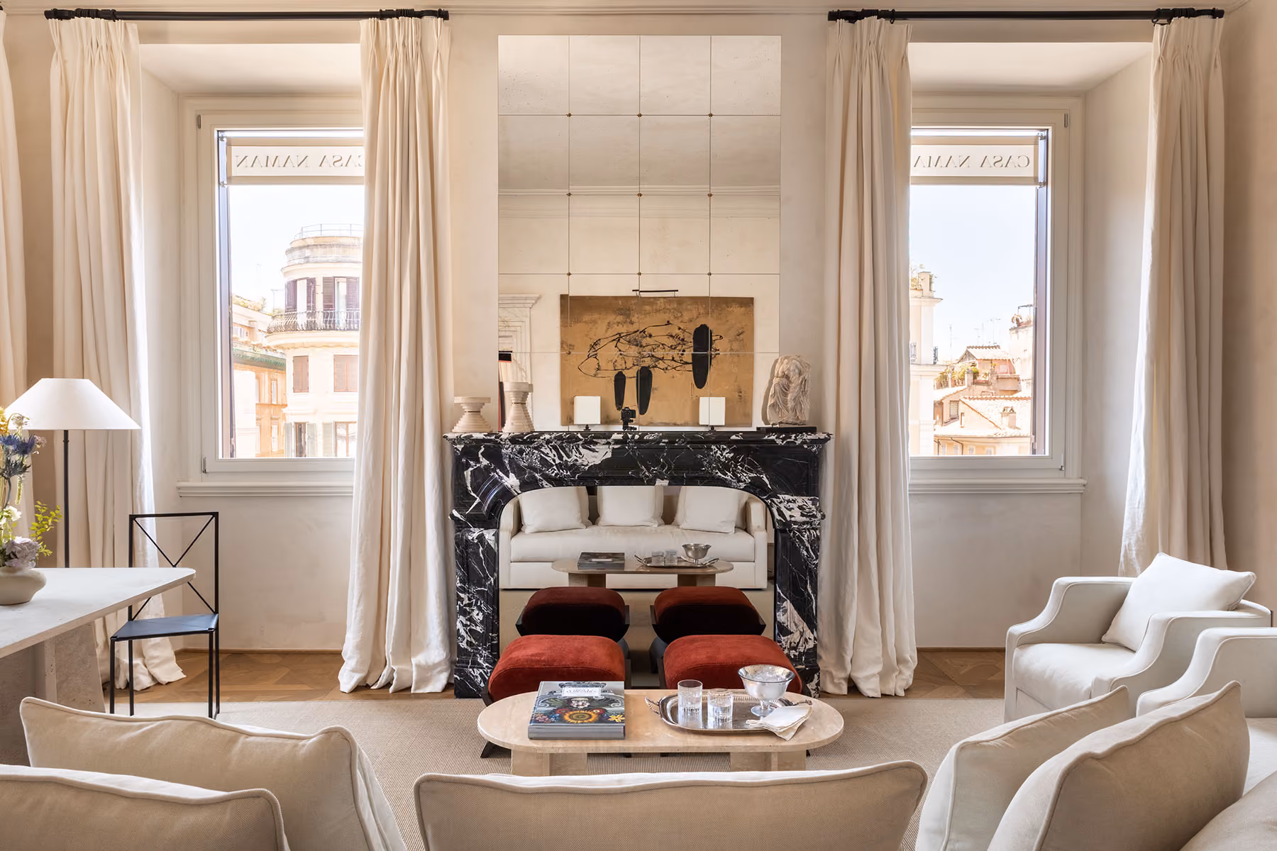 Living room with a black marble fireplace, red ottomans, white armchairs and tall windows