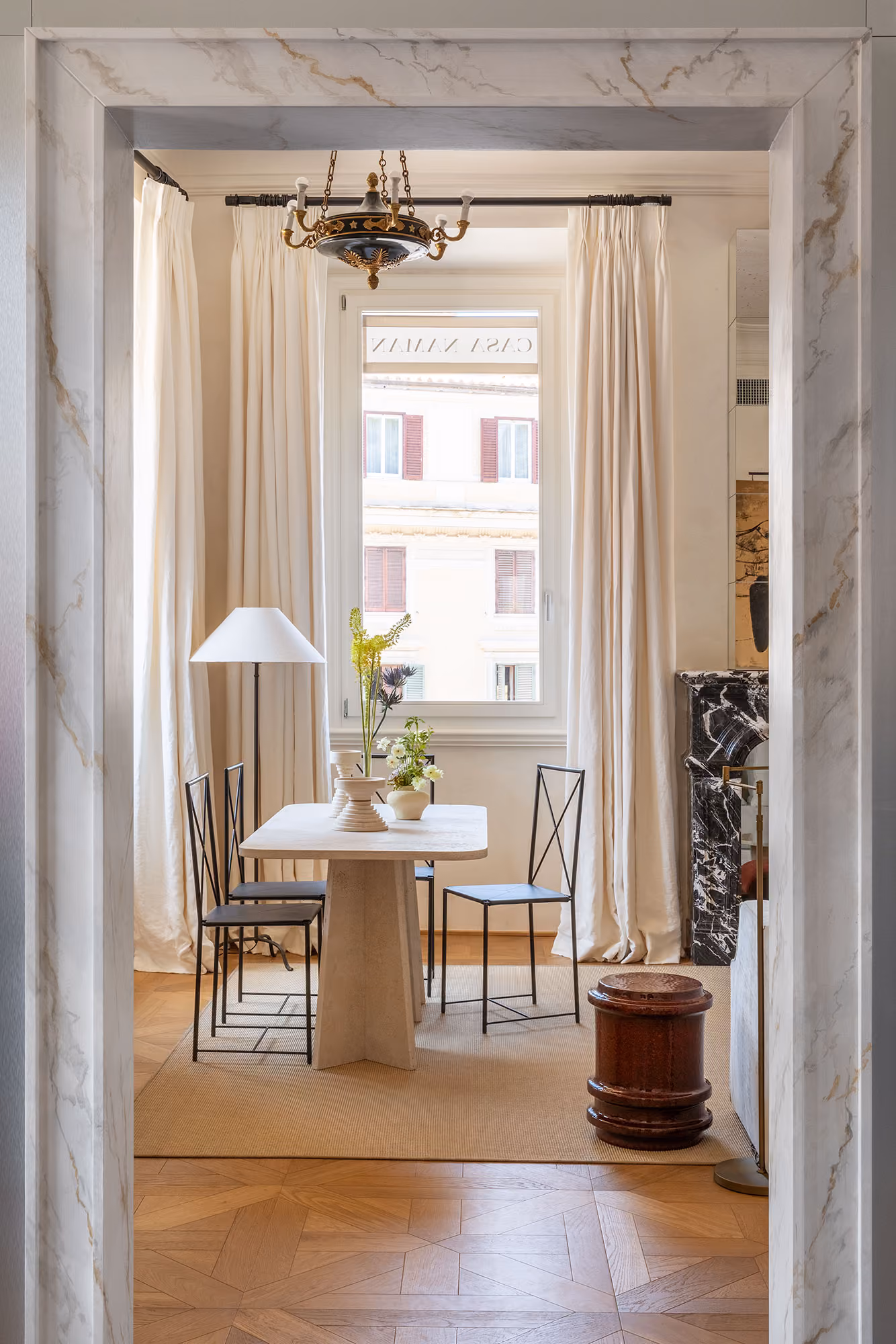 Marble doorway framing a room with sheer curtains, a floor lamp and a dining table with chairs