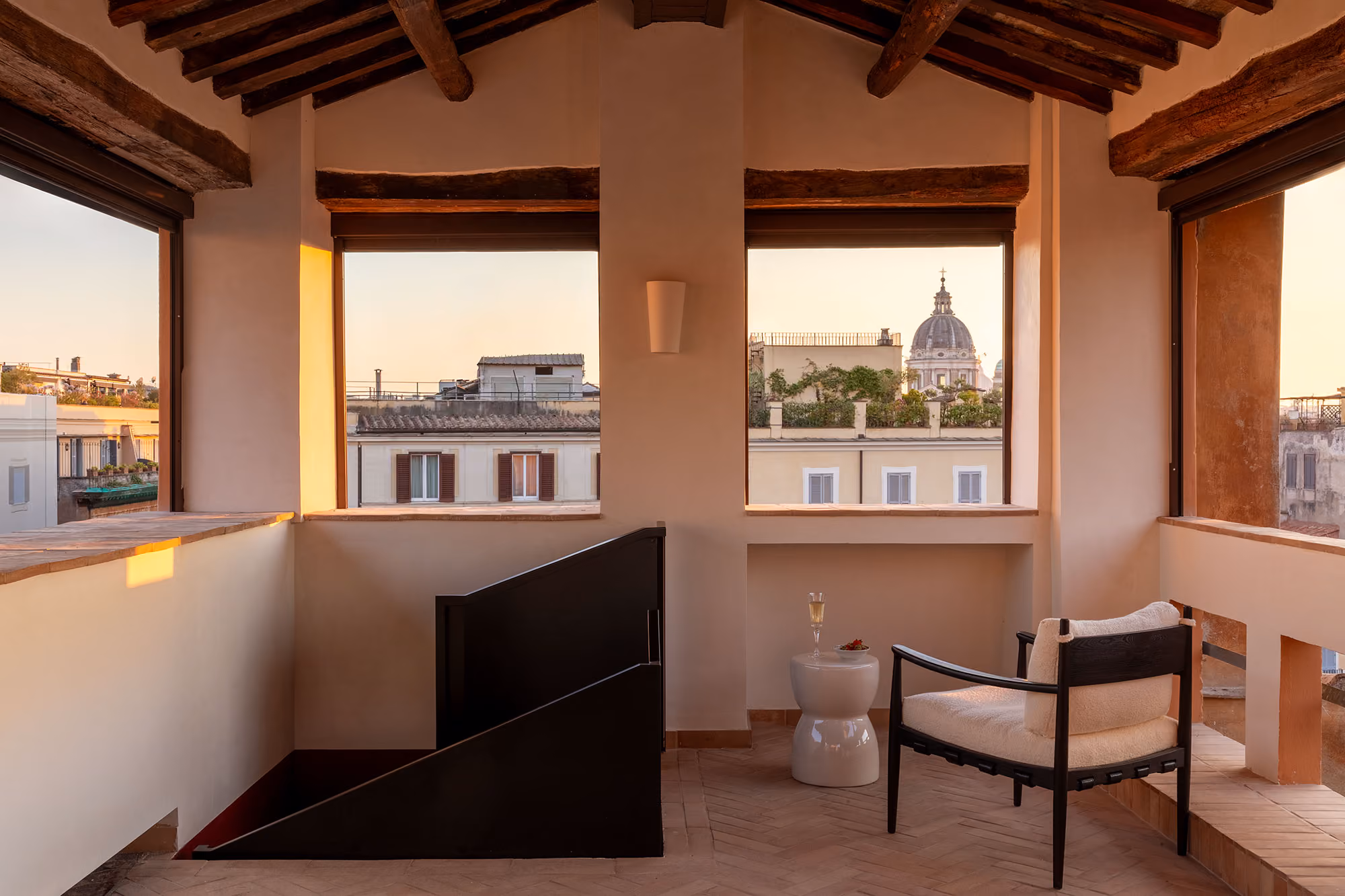 Rooftop attic lounge of the Otium area with exposed wooden beams and windows over Rome's rooftops and a dome
