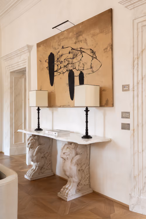 Entrance console with carved marble lion-paw supports, two black lamps and an abstract artwork