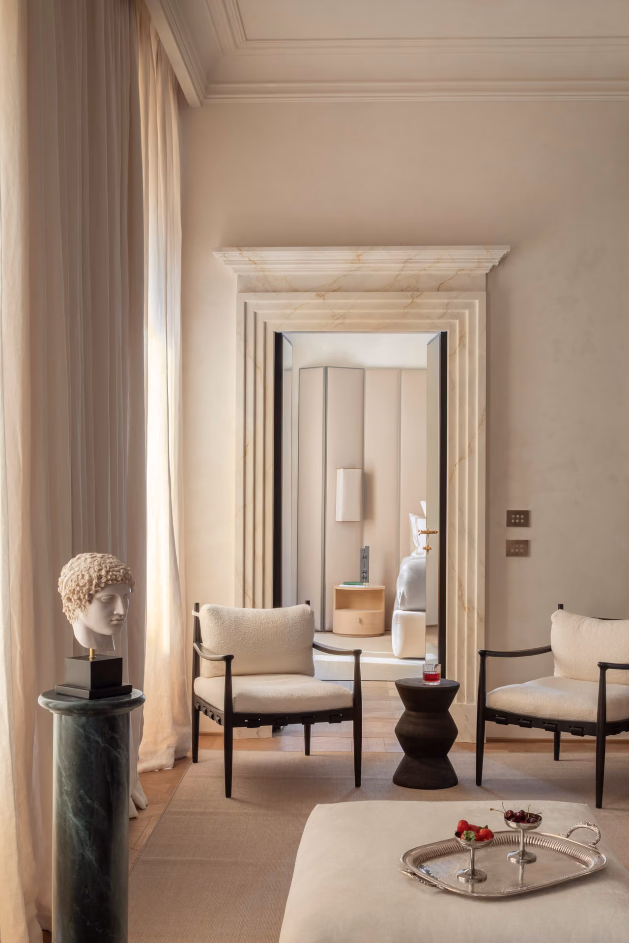 Two armchairs and a small table seen through a marble doorframe into a sitting room