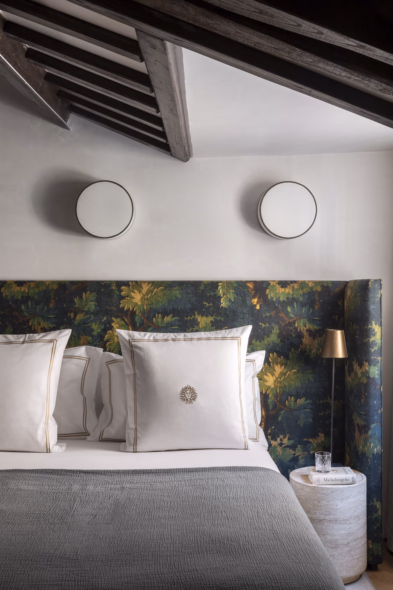 Vesta apartment bedroom with round wall lights, a green botanical headboard and white bedding