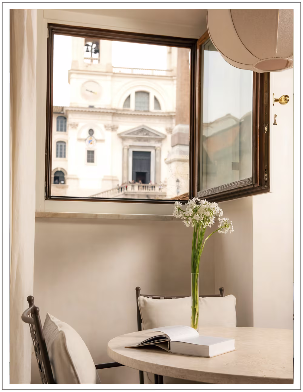 Vesta apartment window overlooking Rome with a vase of white flowers on a small round table