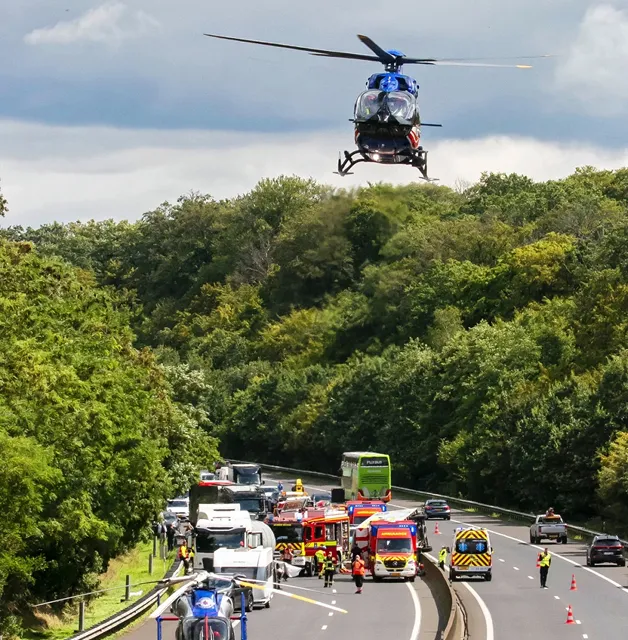 Mehrere Einsatzfahrzeuge und Personal auf einer von Wäldern gesäumten Autobahn, über der ein Hubschrauber als Reaktion auf einen Vorfall schwebt.