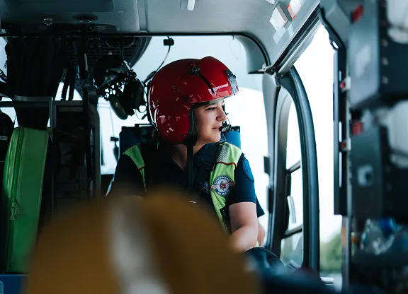 Un secouriste portant un casque rouge et un gilet de sécurité assis à l'intérieur d'un hélicoptère regarde par la fenêtre.