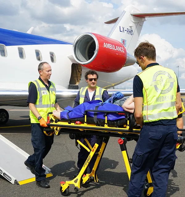 Medizinisches Personal in Warnwesten lädt einen Patienten auf einer Trage in einen Ambulanzjet.