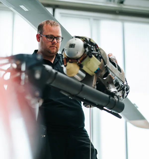 Man wearing glasses inspecting and handling a helicopter engine or rotor assembly indoors.