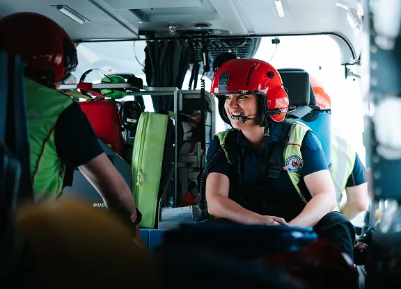 Rescue team members wearing red helmets and safety gear inside a helicopter.