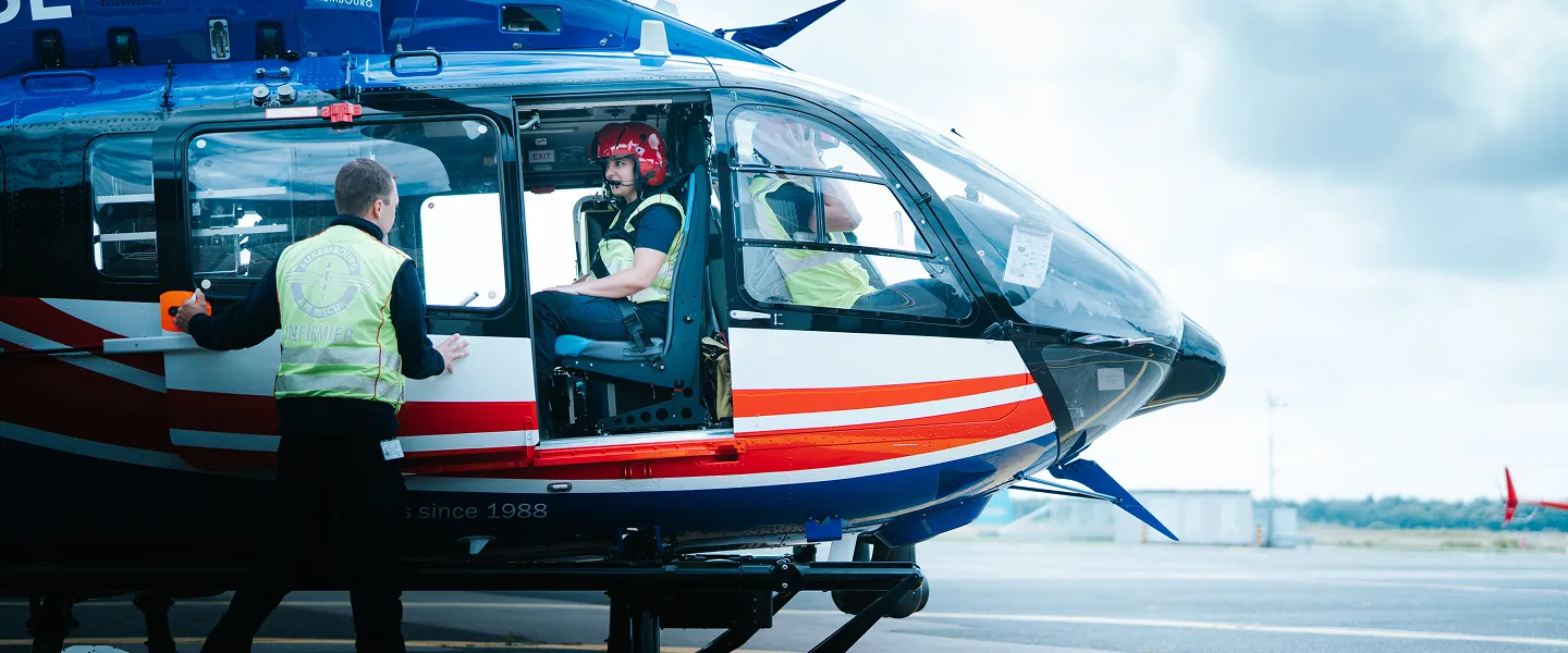 Medical personnel preparing for a helicopter rescue, with one person standing outside and two seated inside the helicopter on a runway.