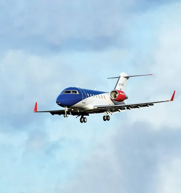 Jet privé à l'avant bleu, à la carrosserie blanche et aux embouts de moteur rouges volant sur un ciel nuageux.