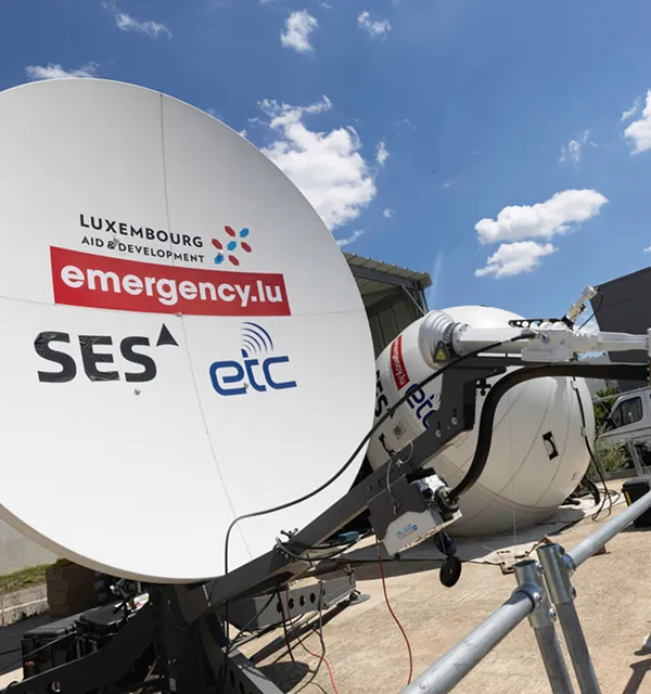 Satellite communication dishes branded with Luxembourg Aid & Development, emergency.lu, SES, and ETC logos under a blue sky with clouds.