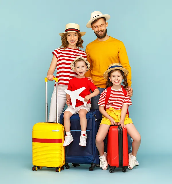 Famille souriante de quatre personnes avec des valises, vêtue de vêtements d'été décontractés et de chapeaux, posant sur fond bleu, prête à voyager.