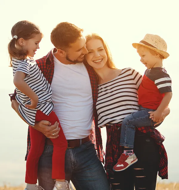 Lächelnde vierköpfige Familie mit Eltern, die ihre kleine Tochter und ihren Sohn bei Sonnenuntergang im Freien halten.