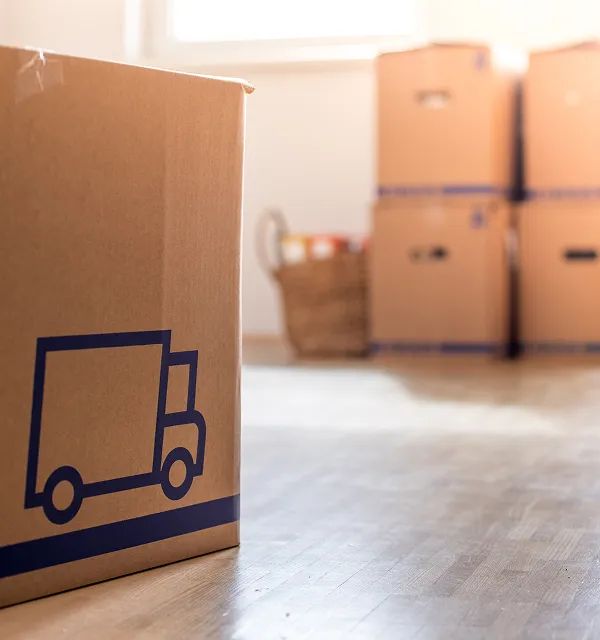 Gros plan d'une boîte de déménagement en carton avec une icône de camion, avec des boîtes de déménagement empilées floues en arrière-plan.