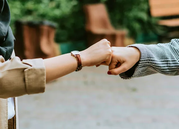 Zwei Personen, die sich im Freien mit verschwommenem Grün im Hintergrund einen Fauststoß geben.