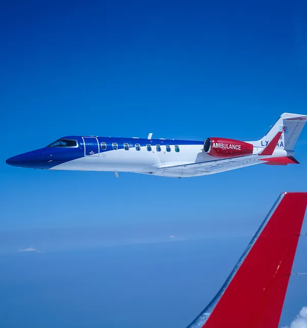 Un avion d'ambulance aérienne médicale volant dans un ciel bleu clair avec une partie d'une autre aile d'avion rouge visible.