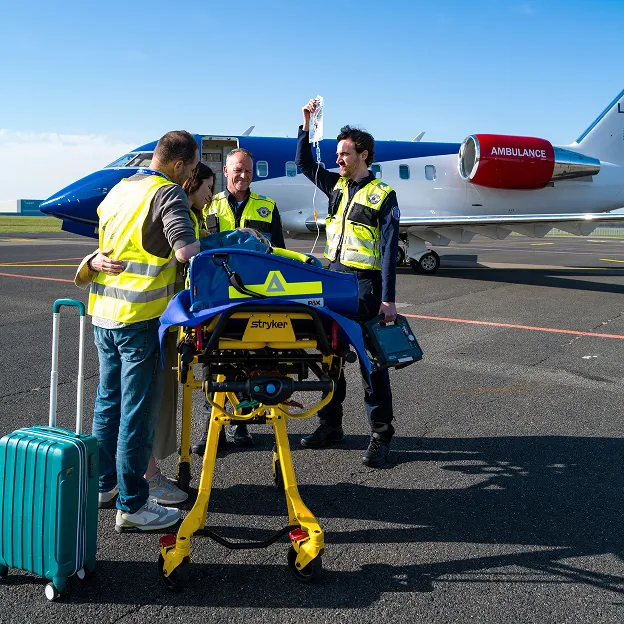 Medical team with a patient on a stretcher next to a small ambulance plane on the tarmac, one medic holding an IV drip.
