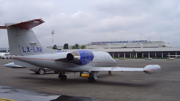 Private jet with registration LX-LAR parked on an airport tarmac with a building labelled 'Halim Perdanakusuma - Jakarta' in the background under an overcast sky.