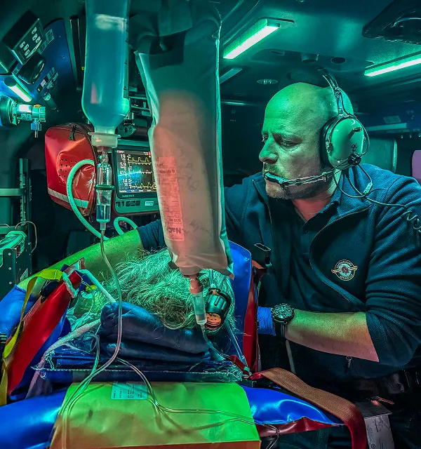 Medical professional in headset providing intensive care to a patient on a stretcher inside an emergency helicopter.