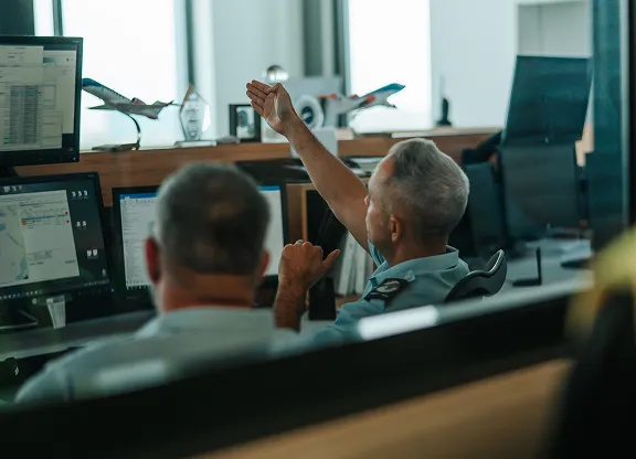 Deux hommes en uniforme travaillant aux postes informatiques d'un bureau, l'un pointant du doigt un écran.
