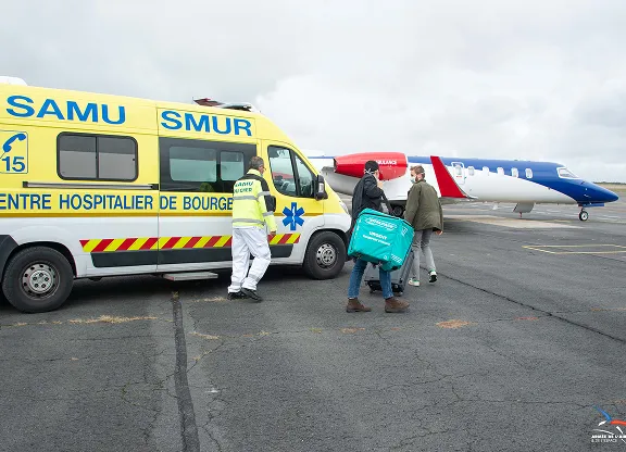 Du personnel médical à côté d'une ambulance jaune du SAMU SMUR et d'un avion-ambulance aérienne rouge, blanc et bleu sur le tarmac.