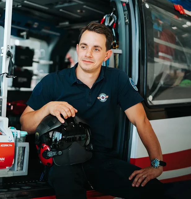 Homme en uniforme de la marine assis sur une marche d'hélicoptère tenant un casque noir et rouge.