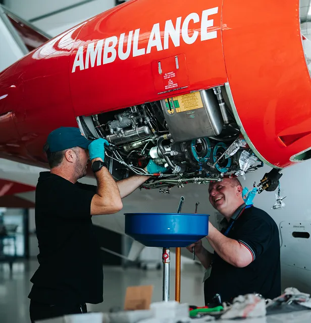 Deux mécaniciens effectuent la maintenance sous le moteur d'un avion-ambulance rouge à l'intérieur d'un hangar.
