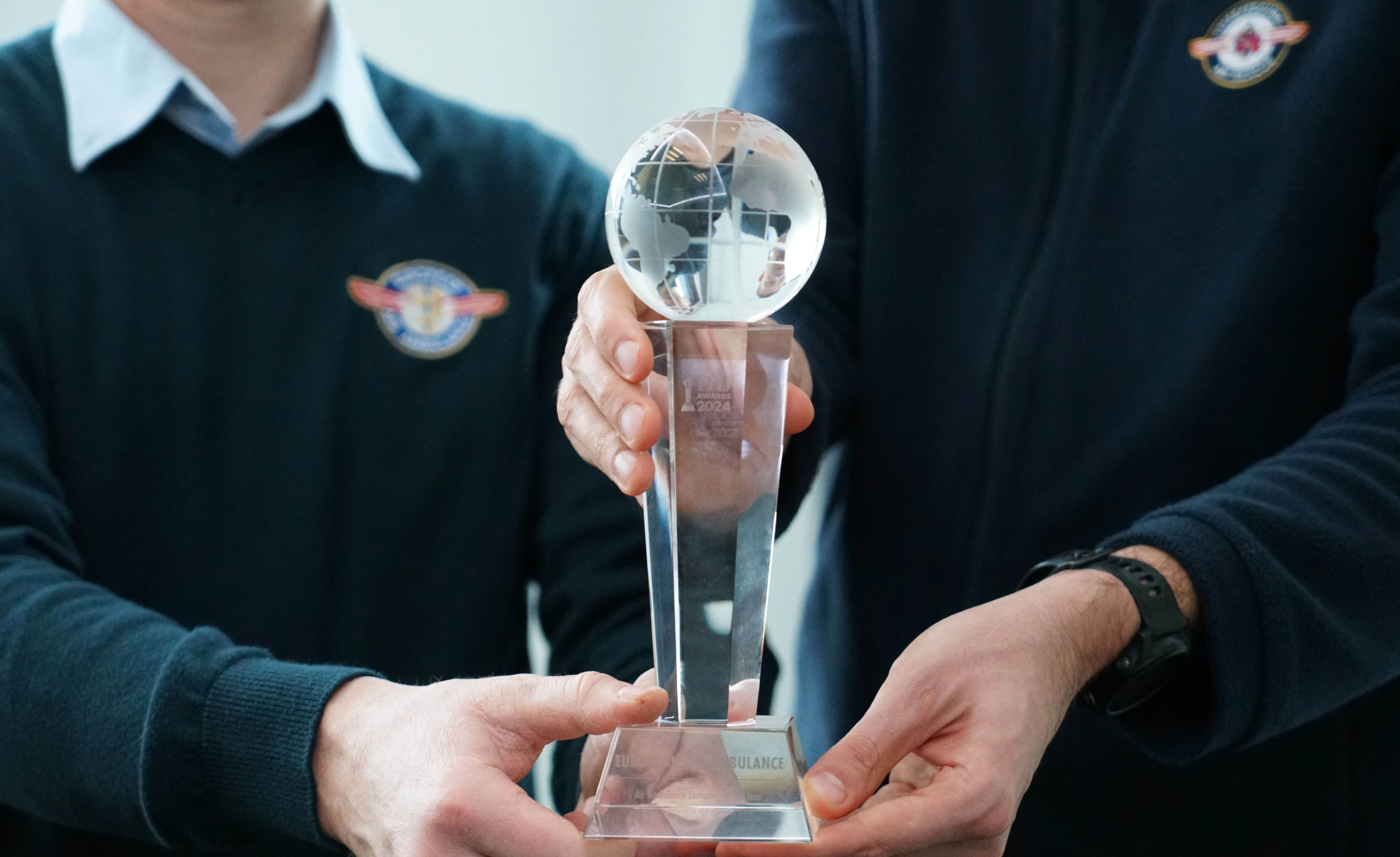 Deux personnes tenant un trophée transparent surmonté d'un globe terrestre, avec le texte « AWARDS 2024 » visible.